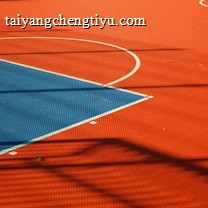 A vibrant sports court with sections of red and blue, featuring crisp white lines marking the boundaries. Shadows from a structure create geometric patterns across the surface, adding depth and interest to the scene.